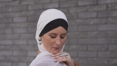 Mavi gözlü genç bir kadının portresi gri tuğla bir duvara karşı tesettürlü.