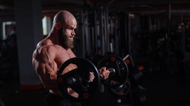 Beyaz, kel, üstsüz bir adam spor salonunda halterle egzersiz yapıyor. Ağırlıklarla bibik bukleler