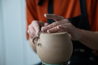 A potter works with a tool on a potters wheel. Close-up of a mans hands
