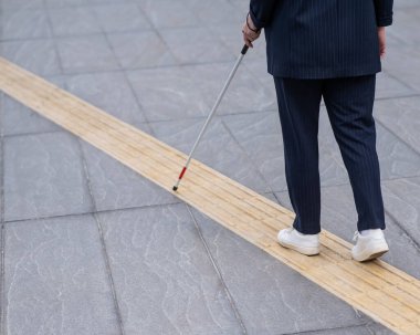 Kör bir iş kadını, değnekle dokunsal fayanslar üzerinde yürüyor.