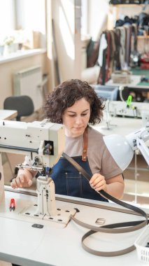 Bir kadın bronzlaştırıcı dikiş makinesine deri kemer dikiyor. Dikey fotoğraf