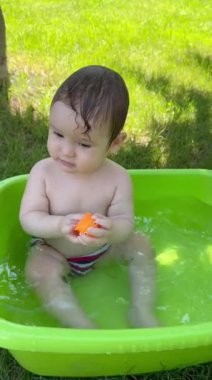 Şirin bir bebek plastik bir havuzda banyo yapar ve yazın dışarıda bir oyuncakla oynar. Dikey video