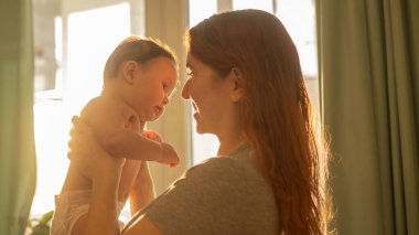 Beyaz bir kadın yeni doğmuş oğlunu nazikçe kaldırır.