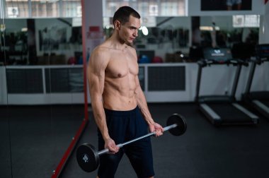 Shirtless man doing bicep exercises with dumbbells in the gym