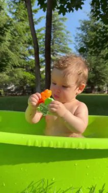 Şirin bir bebek plastik bir havuzda banyo yapar ve yazın dışarıda bir oyuncakla oynar. Dikey video