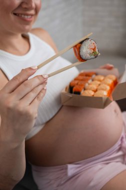 Hamile bir kadın kanepede oturur ve bir kutudan ekmek yer. Yemek teslimatı