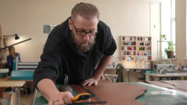 Deri işçisi atölyede deri kesip ölçüyor.