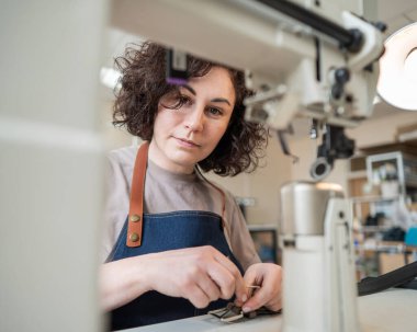 Bir kadın tabakçı dikiş makinesine deri kemer dikiyor.