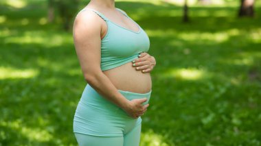 Dışarıda yoga yapan hamile bir kadının göbeğini kapatın.