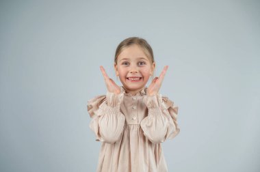 Küçük beyaz kız eğleniyor ve beyaz arka planda surat yapıyor.