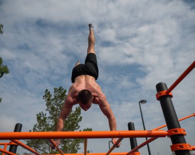Açık hava spor sahasında amuda kalkan genç bir adam. Egzersiz