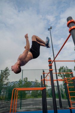 Açık hava spor sahasında ters takla atan genç bir erkek sporcu. Dikey fotoğraf