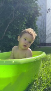 Şirin bir bebek plastik bir havuzda banyo yapar ve yazın dışarıda bir oyuncakla oynar. Dikey video