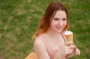 Genç, güzel, kızıl saçlı, diş telleriyle gülümseyen ve dışarıda dondurma yiyen bir kadın.