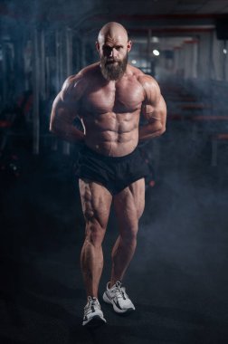 Şort giymiş kaslı kel adam. Vücut geliştirici spor salonunda vücudunu gösteriyor.