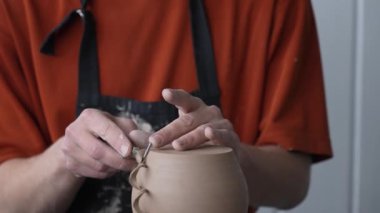 A potter works with a tool on a potters wheel. Close-up of a mans hands