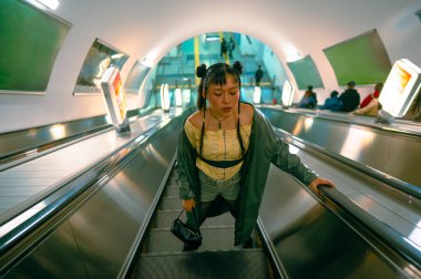 Metroda yürüyen merdivende Asyalı genç bir kadının portresi.