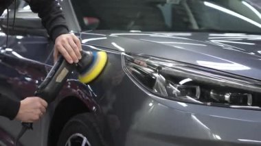 Bir tamirci gri bir arabanın yüzeyini parlatır.