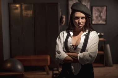 Peaky Blinders tarzı erkek kıyafeti giymiş beyaz bir kadın retro spor salonunda poz veriyor.