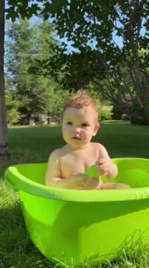 Şirin bir bebek plastik bir havuzda banyo yapar ve yazın dışarıda bir oyuncakla oynar. Dikey video