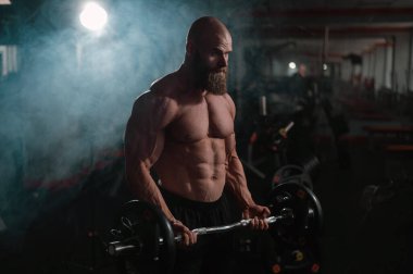 Beyaz, kel, üstsüz bir adam spor salonunda halterle egzersiz yapıyor. Ağırlıklarla bibik bukleler