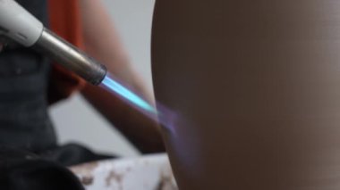 Çömlekçi ellerinin çömlekçi çarkında gaz ocağıyla sürahi ateşlediği yakın plan.
