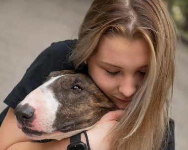 Beyaz kadın portresi açık havada köpeğine sarılıyor.