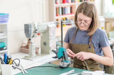 Kadın bronzlaştırıcı bir atölyede deri kemerin kenarlarını inceliyor.