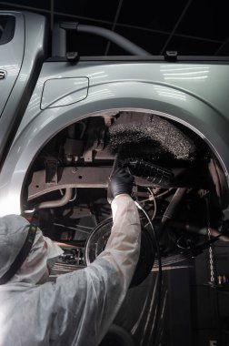 Bir otomobil tamircisi korozyon önleyici maddeyi arabanın alt gövdesine uygular.