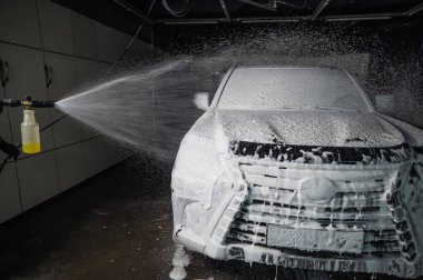 Oto yıkamada siyah arabaya köpük süren bir adam.