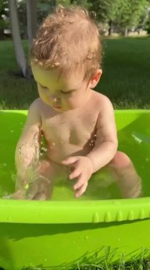 Şirin bir bebek plastik bir havuzda banyo yapar ve yazın dışarıda bir oyuncakla oynar. Dikey video