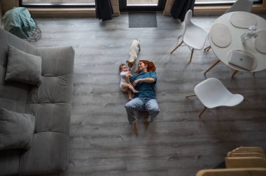 Beyaz kadın, oğlu ve Jack Russell Terrier köpeğiyle yerde yatıyor.