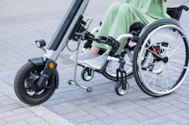 Tekerlekli sandalyedeki yüzü olmayan ve manuel kontrol için yardımcı bir aleti olan bir kadın. Elektrikli bisiklet.