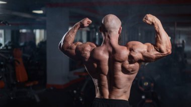 Tişörtsüz poz veren kaslı kel adam. Vücut geliştirici spor salonunda sırt kaslarını gösteriyor.