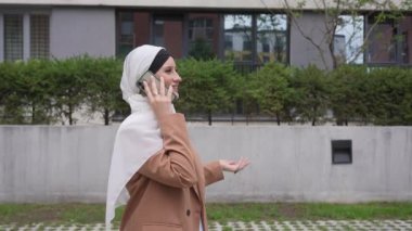 Açık havada akıllı telefondan konuşan tesettürlü genç kadın.