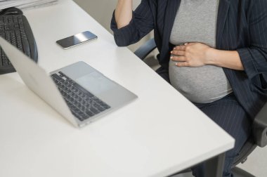 Hamile bir kadın ofiste dizüstü bilgisayarda çalışıyor. Karnına yakın çekim.