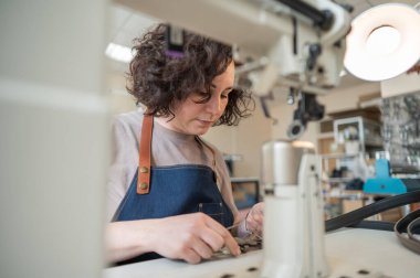 Bir kadın tabakçı dikiş makinesine deri kemer dikiyor.