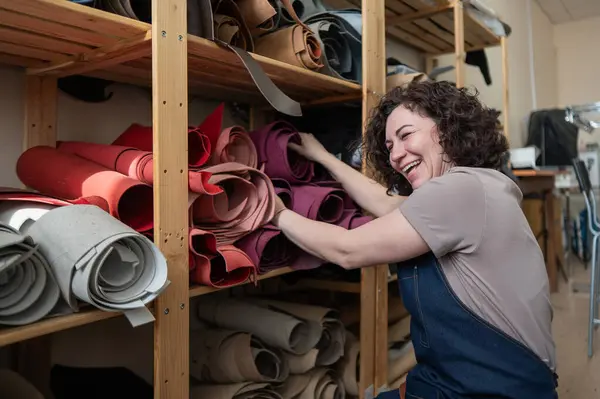 stock image Woman leatherworker selects a roll of leather in the workshop