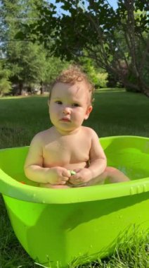 Şirin bir bebek plastik bir havuzda banyo yapar ve yazın dışarıda bir oyuncakla oynar. Dikey video