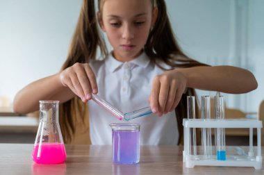 Liseli bir kız kimya dersinde deneyler yapıyor. Beher kabından renkli sıvılar döken bir kız.