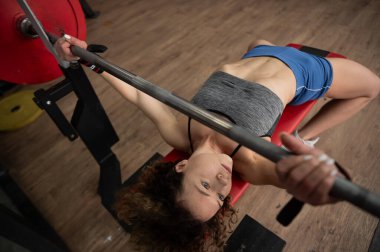 Orta yaşlı bir kadın spor salonunda göğüs presi yapıyor.