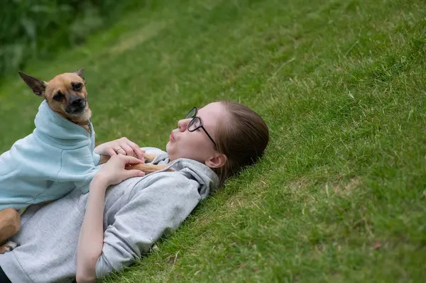 Küçük bir köpekle yürürken çimenlerde yatan beyaz bir kadın.