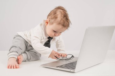 Takım elbiseli şirin bir çocuk gözlük takıyor ve dizüstü bilgisayarın arkasında yatıyor.