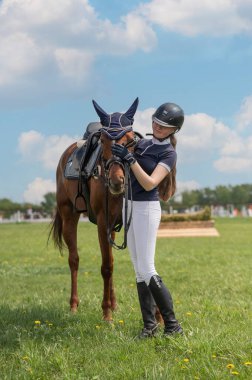 Genç bir kız bir binicilik yarışmasının önünde bir atın yanında duruyor. Dikey fotoğraf