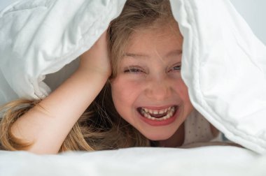 Küçük şirin bir kızın portresi. Battaniyenin altında gülüyor ve saklanıyor.