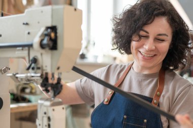 A woman tanner sews a leather belt on a sewing machine clipart