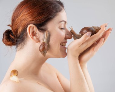 Büyük bir salyangoz tutan beyaz bir kadının yakın çekimi. Kozmetolojide kabuklu deniz hayvanı kullanımı