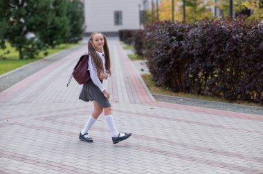 Üniformalı ve sırt çantalı mutlu beyaz kız okuldan sonra dışarı atlıyor.