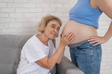 Yaşlı bir kadın hamile kızının karnına yaslanır. Yakın plan.