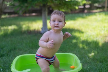 Tatlı erkek bebek yazın havuzda yıkanır.